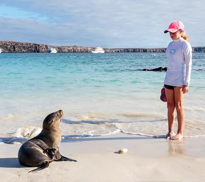 Young lady standing next to a Galapagos sea lion at shore