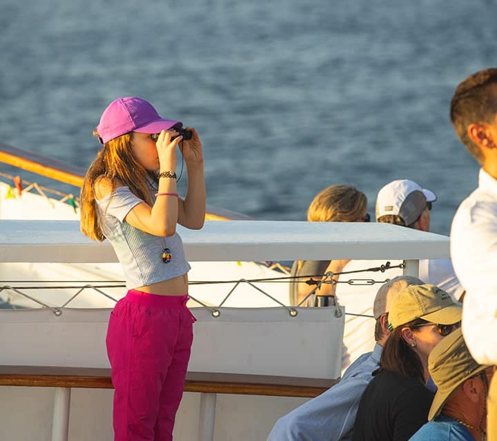 Young girl using binoculars to see Galapagos Islands afar from a Quasar Yacht