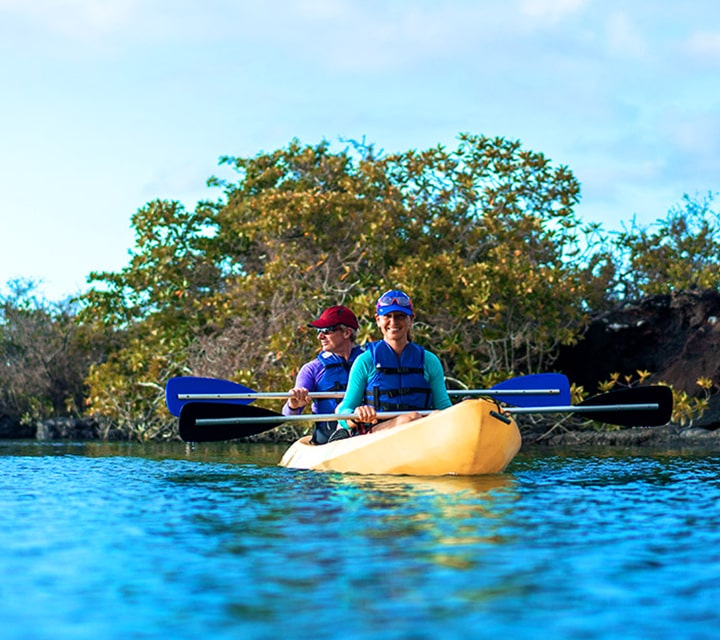 Kayakers pose for a picture while on a yellow kayak at Elizabeth Bay in the Galapagos Islands