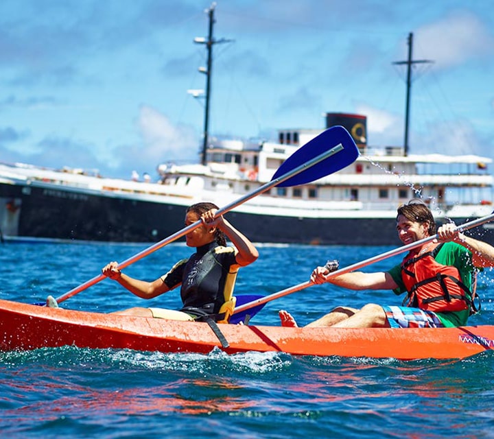 A couple on an orange kayak together paddling next to Quasar's Evolution Yacht