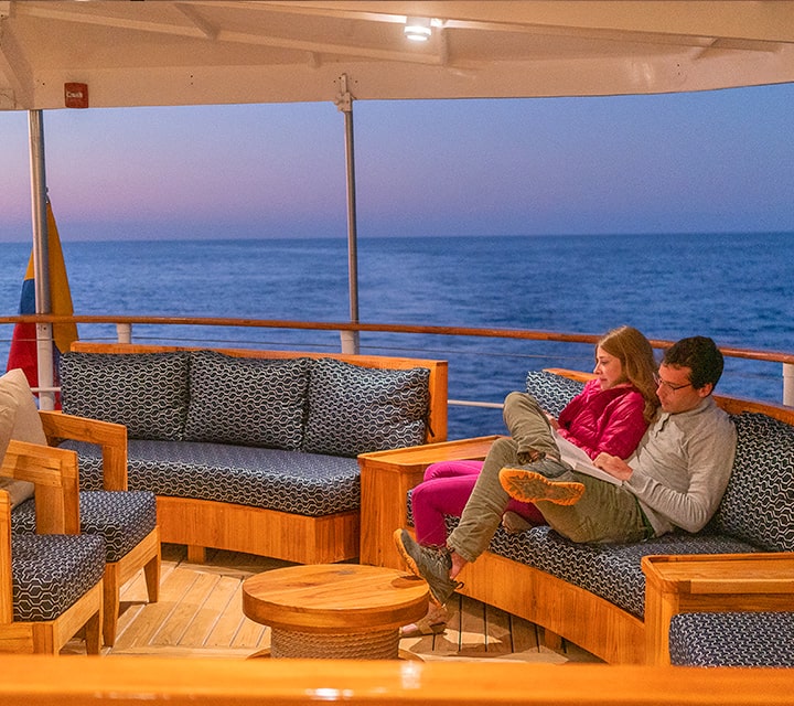 A couple lounging on the upper deck of Quasar's luxury Evolution yacht on a 8-day cruise