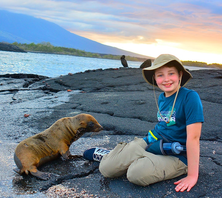 A boy sitting next to a Galapagos Sea Lion and other wildlife in the Galapagos Islands